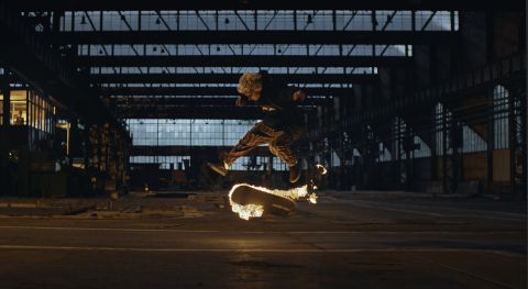 Zdjęcie przedstawia kadr z filmu w ramach Wrooklyn ZOO DCF. W opuszczonym hangarze młody człowiek wyskoczył do góry na swojej deskorolce. Deskorolka płonie żywym ogniem.