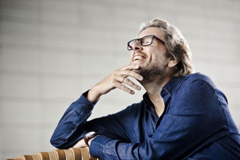 Mężczyzna w okularach i niebiweskiej koszuli siedzi uśmiechnięty na ławce. Źródło: informacja prasowa NFM we Wrocławiu_Micha-Nesterowicz-01-Lukasz-Rajchert-10-11-2017