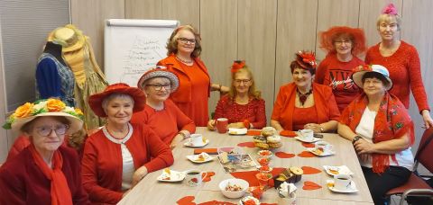 Na zdjęciu grupa pań ubranych na czerwono, przed nimi na stole walentynkowe dekoracje