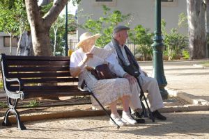 Na zdjęciu para seniorów siedzi na ławeczce w parku