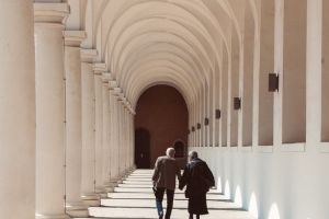 Na zdjęciu dwie osoby starsze idące pod arkadami. 