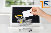 laptop ręka trzymająca białą pustą kartę oraz miniaturka wózka na zakupy 