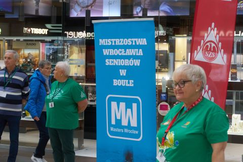 Dwie kobiety z drużyn w bule przy banerach organizatorów.