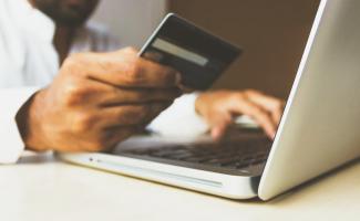 Zdjęcie przedstawia ręce trzymające kartę oraz laptopa