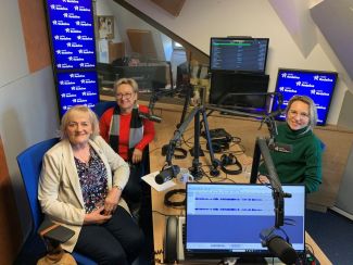 Trzy Panie siedzące przy stole i mikrofonach w studiu radiowym.