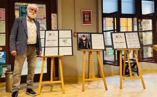 Mirosław Wojtowicz przy sztalugach na których wystawione są grafiki.