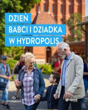 Plakat promujący wydarzenie „Dzień Babci i Dziadka w Hydropolis”. Na pierwszym planie starsza kobieta i mężczyzna (babcia i dziadek) trzymający za ręce wnuka, spacerujący w słoneczny dzień. W tle ceglana architektura oraz osoby zwiedzające. Logo Hydropolis i MPWiK Wrocław w dolnej części. Kolorystyka: niebieskie napisy na tle jasnych i naturalnych barw. Tematyka: atrakcje rodzinne w Hydropolis.