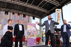 Dni Seniora 2023 Rynek we Wrocławiu. Na scenie Prezydent wręcza symboliczny klucz Parze Królewskiej. Obok stoi prowadzący.