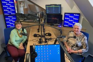 Dwie panie przy stole przy mikrofonach w studiu radiowym.