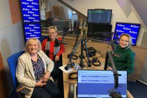 Trzy Panie siedzące przy stole i mikrofonach w studiu radiowym.