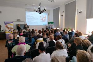 Na zdjęciu w sali konferencyjnej siedzące osoby na krzesłach podczas prezentacji Dni Seniora 2025. 