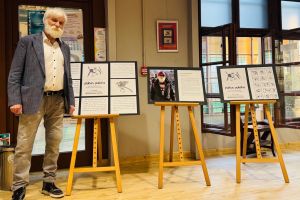 Mirosław Wojtowicz przy sztalugach na których wystawione są grafiki.