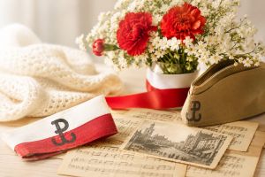 Biało-czerwone kwiaty, nuty i opaska z symbolem Polski Walczącej tworzą ciepłą, patriotyczną kompozycję nawiązującą do powstańczych pieśni i wspomnień.